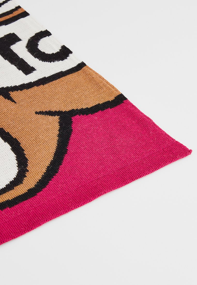 Ecke eines gestrickten Stoffes in Schwarz, Weiß, Braun und Rosa, die eine teilweise Grafik und Text auf einem einfarbigen Hintergrund bilden.