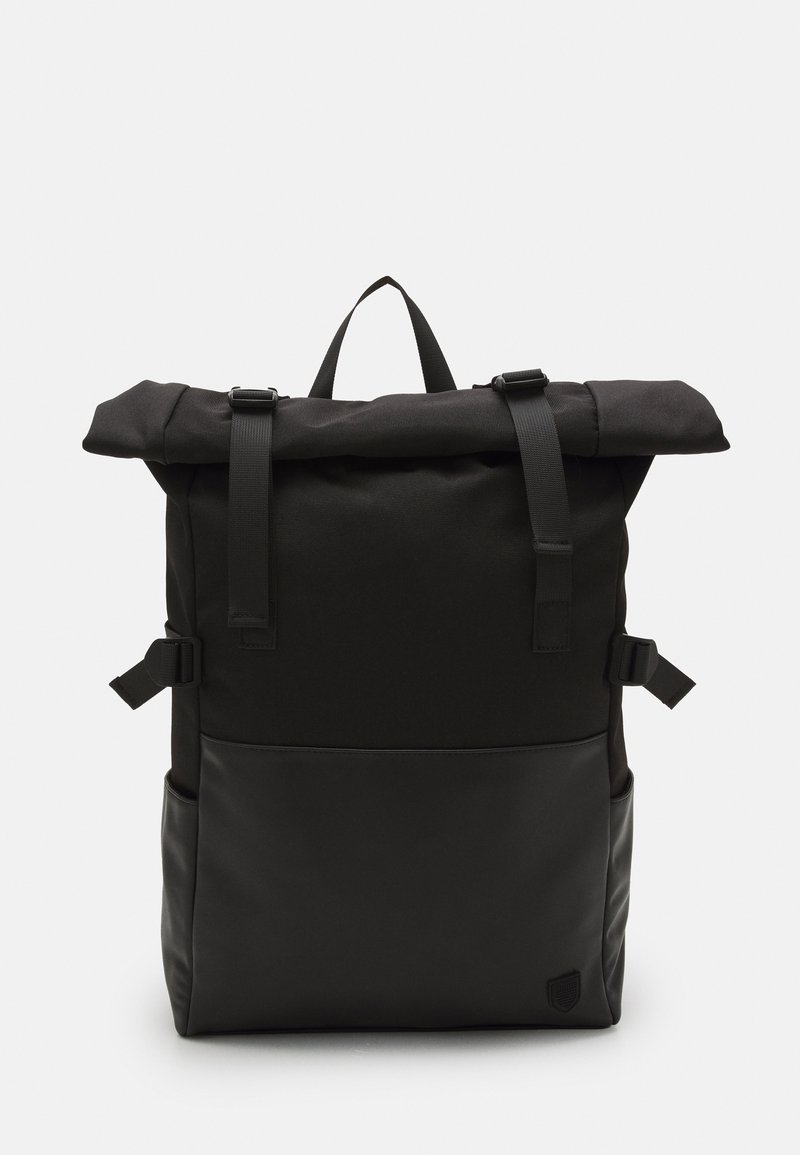 Sac à dos noir à rouleau avec bretelles réglables, boucles latérales et un petit emblème dans le coin inférieur droit.