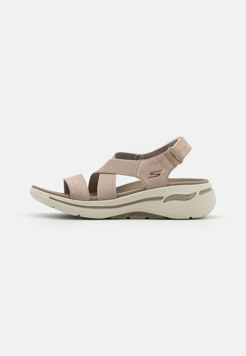 Beige klittenbandsandalen met brede kruislijnen, zacht suede bovenwerk, gevoerde voetbed en een lichte, gebogen rubberen zool.