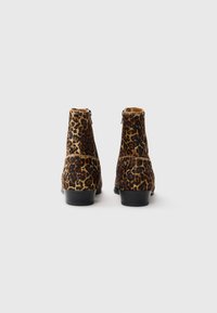 Bottines à imprimé léopard en matériau doux et texturé, avec des semelles en caoutchouc noires. Fermeture éclair à l'arrière pour un enfilage facile. Design à bout rond.