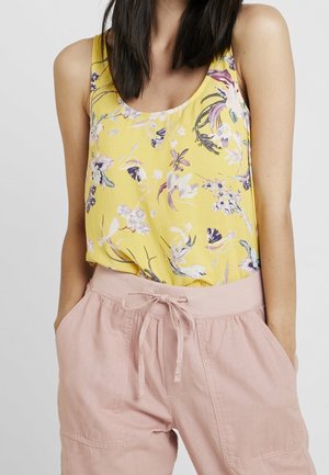Top de tirantes amarillo con estampado floral, hecho de una tela ligera, que presenta un escote redondeado y un corte holgado. Combinado con pantalones cortos rosas claros con cordón.
