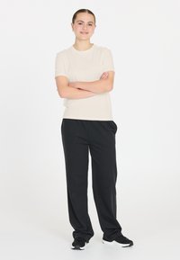 Beige kortärmad t-shirt med rund hals, kombinerad med lösa svarta byxor och svarta träningsskor; mjukt tyg och avslappnad passform.