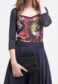 Top a fantasia floreale con maniche corte blu navy, abbinato a una gonna blu navy semplice. Clutch in suede nero con flap pieghevole tenuta in mano.