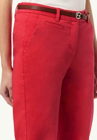 Rote Baumwollhosen mit schlanker Passform, ausgestattet mit einem braunen Ledergürtel und einer silbernen Schnalle. Enthält seitliche Taschen und ein schlichtes Frontdesign.