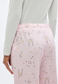 Ροζ ανοιχτό παντελόνι πυτζάμας με απαλό υφή, διακοσμημένο με σχέδιο από ποτήρια σαμπάνιας, μαύρο κονφετί και χρυσά αστέρια κατά μήκος της μέσης.