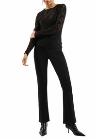 Schwarzes Spitzenoberteil mit langen Ärmeln, das mit floralen Mustern verziert ist, kombiniert mit schwarzen Schlagjeans und spitzen schwarzen Stiefeletten mit Absatz.