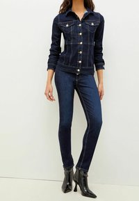 Mörkblå denimjacka med knappstängning och två bröstfickor, i kombination med figursydda mörka denimbyxor och glänsande svarta ankelstövlar.