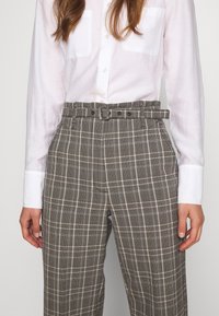 Grå rutiga byxor med hög midja, med bälte, i vida ben och sidofickor. Materialet verkar lätt och texturerat.