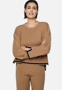 Bruine gebreide sweatshirt met een boxy snit, voorzien van marineblauwe afwerking op de mouwen en de zoom. De stof heeft een zachte textuur.