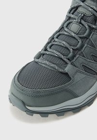 Scarpa da hiking grigia con tomaia in rete e suede, dotata di lacci testurizzati e suola in gomma resistente, progettata per attività all'aperto.
