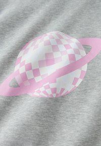 Planète à damiers rose et blanc avec un anneau autour, imprimée sur un tissu gris clair, montrant la texture et les plis du tissu.