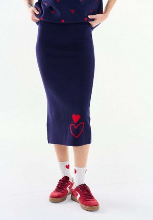 Osoba ubrana w granatową spódnicę w czerwone serca, białe skarpetki w czerwone serca, czerwone trampki oraz granatową bluzkę z czerwonymi wzorami serc.