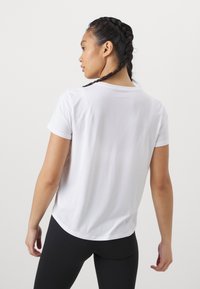 Valge lühikeste varrukatega spordisärk, sileda tekstuuriga, ümar kaelusega ja lahtise lõikega, kombineeritud mustade retuusidega.