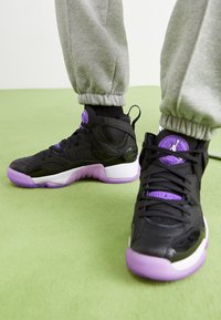Svarta sneakers med lila detaljer, med en texturerad ovandel, vit mellansula och lila genomskinlig sula. Rundad design med snörning.