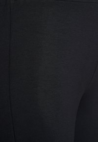 Schwarze Leggings aus glattem, dehnbarem Material. Die Oberfläche hat eine dezente Struktur ohne sichtbare Muster oder Verzierungen.