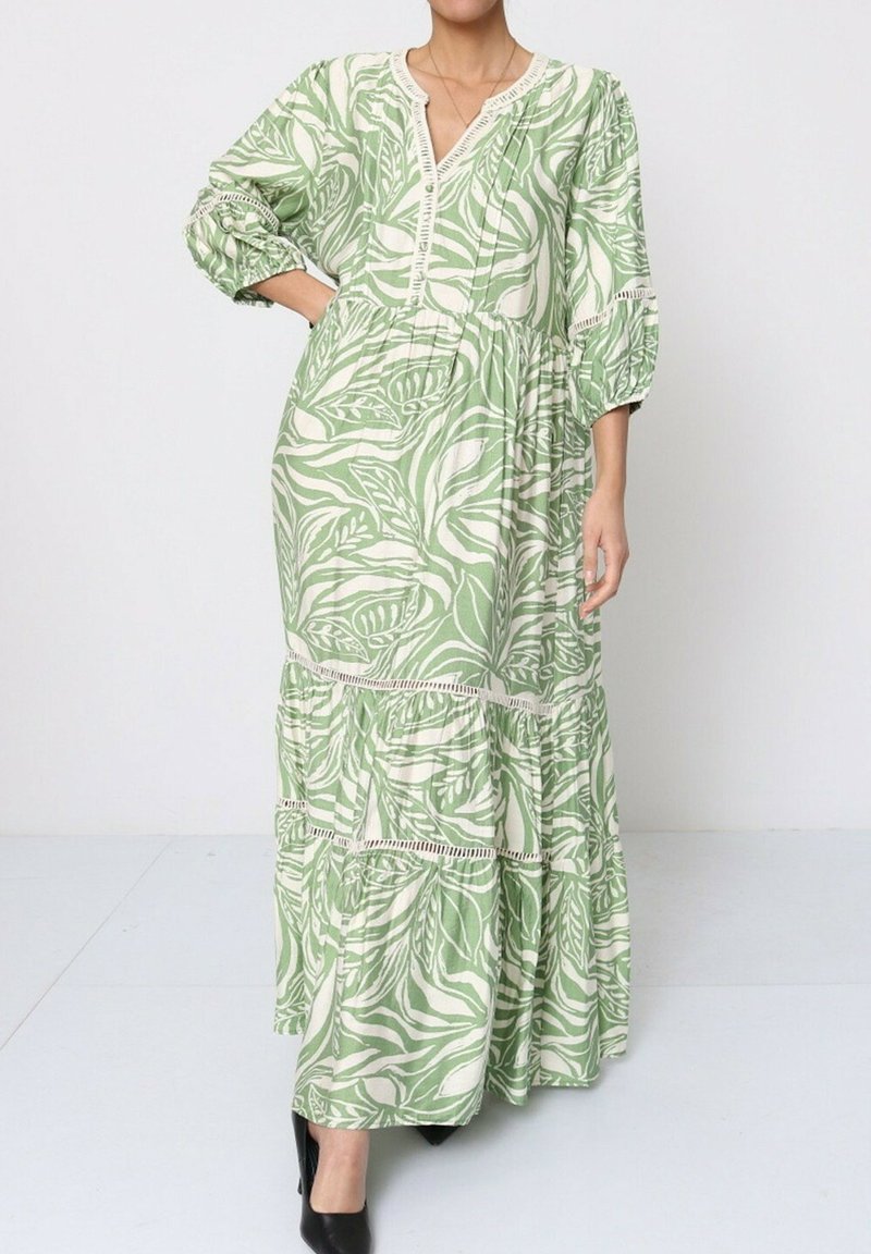 La robe maxi présente un motif de feuilles vertes et blanches, un décolleté en V, une taille froncée et une jupe à volants. Fabriquée en tissu léger avec des manches ballon.