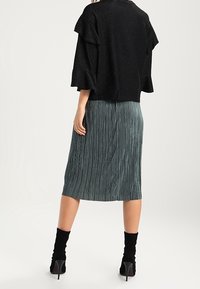 Top negro texturizado con mangas con volantes, combinado con una falda midi plisada verde. Botines negros completan el look.