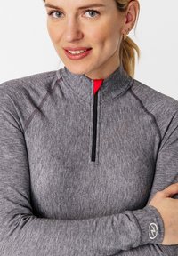 Grau langärmliges Oberteil mit einem halben Reißverschluss, ausgestattet mit roten Akzenten und schwarzem Nähen. Das Logo am Bund verleiht dem sportlichen Look das gewisse Etwas.