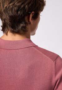 Maglione a maniche corte con colletto in tessuto lavorato rosa, caratterizzato da una finitura texturizzata e cuciture visibili lungo le cuciture delle spalle.