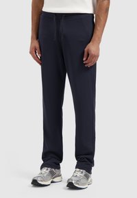 Navyblauwe sweatpants van zachte stof, met een trekkoord in de taille, taps toelopende broekspijpen en zijnaden. Draag het met zilverkleurige hardloopschoenen.