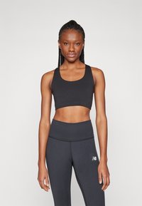 Top deportivo negro de corte corto con tirantes gruesos, combinado con leggings negros de cintura alta que tienen un pequeño logo blanco en el muslo izquierdo.