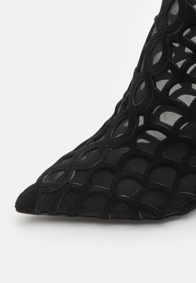 Pantof cu toc înalt negru, cu vârful ascuțit, având un overlay din plasă și accente din suede, prezentând un model geometric cu decupaje.