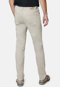 Jeans beige claro con corte recto, que cuentan con bolsillos traseros y una etiqueta de cuero con marca en la cintura, usados con zapatos marrones.