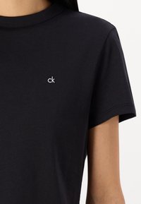T-shirt in cotone nero con maniche corte e colletto rotondo. Presenta un piccolo logo ricamato in bianco "ck" sul lato sinistro del petto.