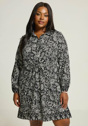 Mustavalkoinen paisley-kuvioinen mekko, jossa on kauluskääntö, pitkät hihat ja sidottu vyötärö, sekä liehuva helma ja teksturoitu kangas.