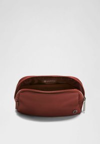 Crvena najlonska torbica s glatkom teksturom i zatvaranjem na patentni zatvarač. Unutrašnjost sadrži mrežastu džep. Logo brenda vidljiv je sa strane.