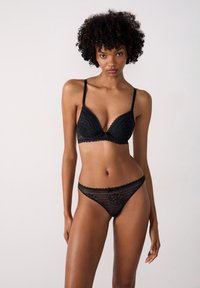Zwart kanten lingerie set bestaande uit een gepadded beha met golvende randen en een bijpassende string met bloempatronen en ingewikkelde details.