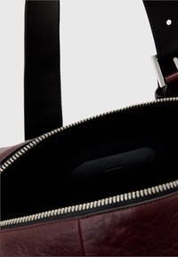 Maroon leather bag with a smooth texture, featuring a silver zipper closure and a black interior. Includes a small black pocket inside.