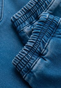 Dettaglio di tessuto blu con polsini elasticizzati arricciati, che mostra una texture liscia con lievi variazioni di tono e linee di cucitura.