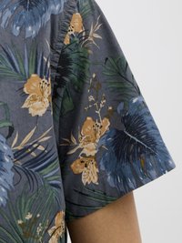 Chemise à manches courtes en tissu gris foncé, ornée d'un motif floral bleu, jaune et vert, avec des accents feuillus et une texture douce.