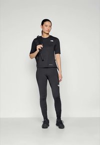 Μαύρη αθλητική ενδυμασία που περιλαμβάνει κοντομάνικη εφαρμοστή μπλούζα και κολάν, φτιαγμένα από ελαστικό υλικό, σε συνδυασμό με μαύρα υποδήματα και μπατόν πεζοπορίας.