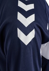 Marineblåt stof med fire hvide nedadvendte chevron-striber i en lodret linje på et ærme.