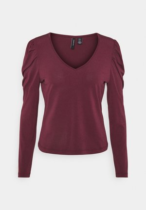 Haut à manches longues bordeaux pour femme avec décolleté en V et légères volants sur les épaules, taille cintrée et tissu lisse.