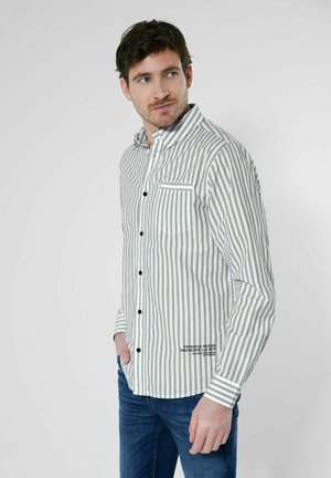 Gestreept overhemd in wit en zwart, met een borstzak, zwarte knopen en contrasterende manchetten, gecombineerd met blauwe jeans.