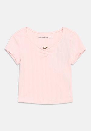 Haut pour tout-petit en maille côtelée rose pâle à manches courtes, avec un léger col en V et un petit détail de boucle en tissu au centre devant.