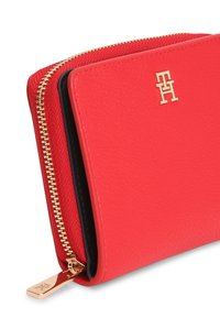 Κόκκινο δερμάτινο πορτοφόλι με χρυστό φερμουάρ και μεταλλικά στοιχεία. Διαθέτει υφή στην επιφάνεια και ανάγλυφο λογότυπο στο μπροστινό μέρος. Εσωτερική επένδυση μαύρου χρώματος.