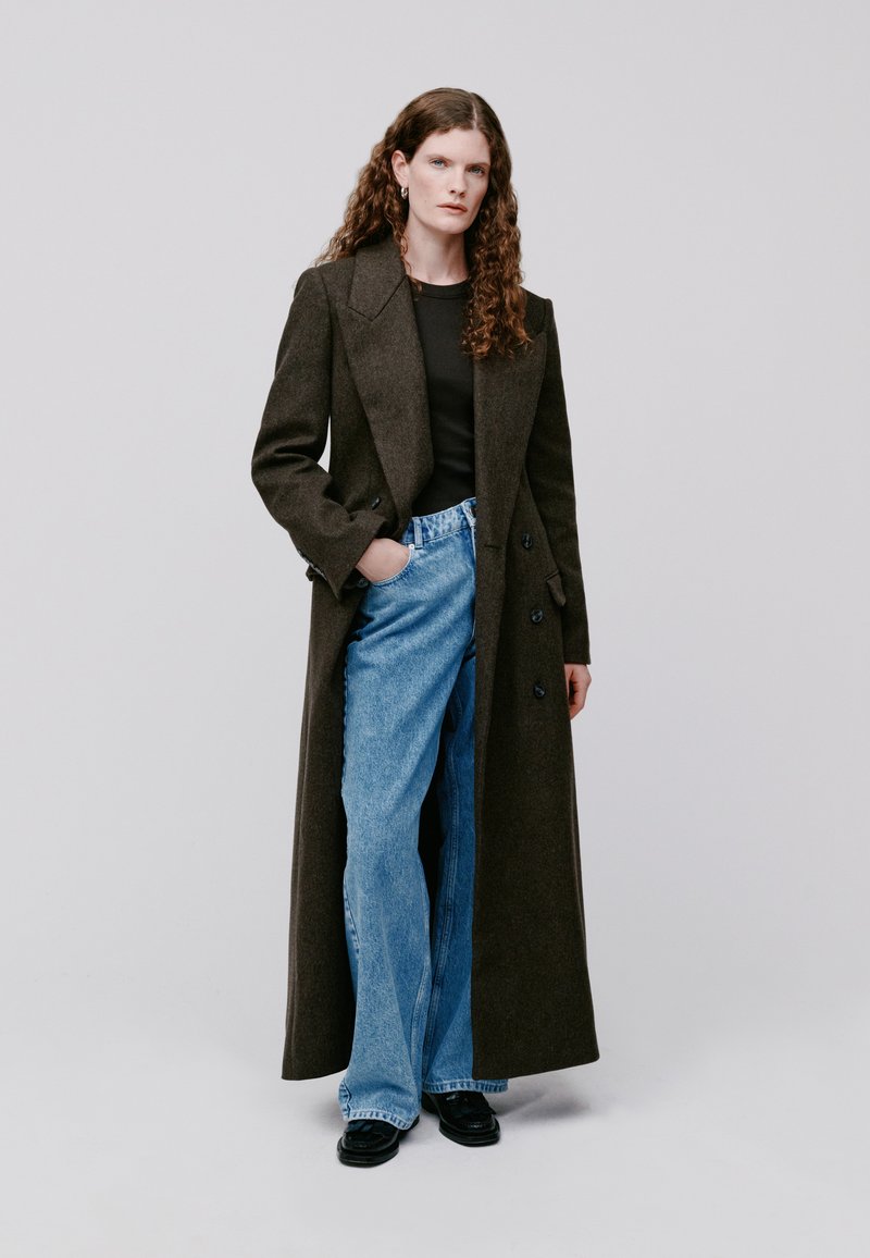 Lange bruine wollen jas met notch lapels, dubbele knopen aan de voorkant; gecombineerd met lichtblauwe high-waisted denim jeans en zwarte schoenen.