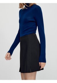 Maglione a collo alto blu navy con maniche lunghe abbinato a una gonna nera svasata con spacchi laterali e una texture liscia.