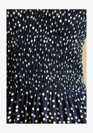 Marineblåt stof med hvide polkaprikker har smocket elastisk syning, der skaber en rynket tekstur på kjolens midtersektion.