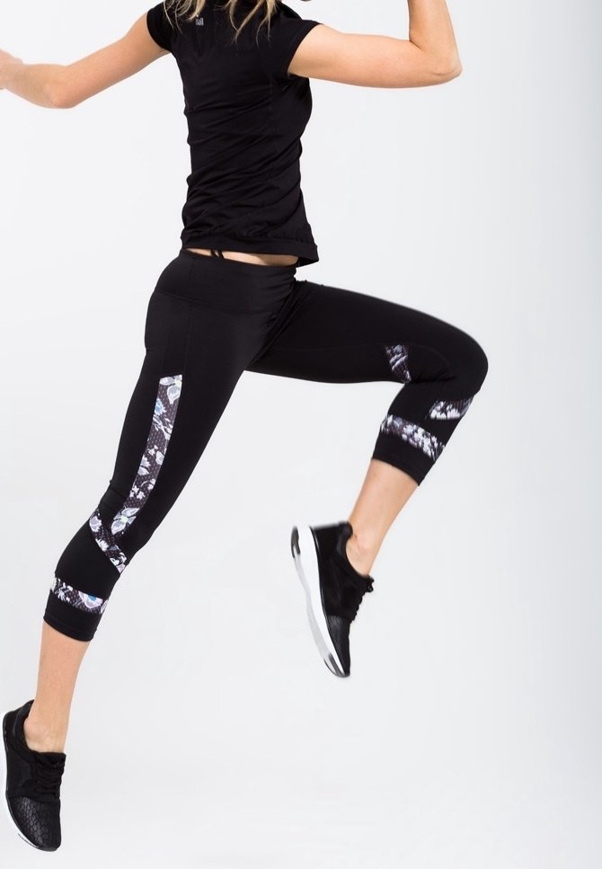 Leggings deportivos negros con acentos estampados, combinados con una camiseta ajustada negra. Los leggings tienen paneles laterales y un diseño elegante.