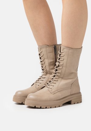 Beige Leder-Ankle-Boots mit Schnürung vorne und seitlichem Reißverschluss. Strukturierte Oberfläche, klobige Gummisohle, verstärkte Zehenpartie und minimale Nähte.
