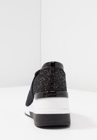 Sneaker nera con un tallone testurizzato e luccicante, corpo in rete nera elegante e una suola intermedia bianca con suola in gomma nera.