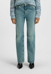 Ljust blå denimjeans med rak passform, femficksdesign och fransad fåll, i kombination med spetsiga svarta ankelskor. Texturerad yta.