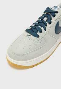 Gray suede and leather sneaker with navy laces, perforated toe, and rubber gum sole; features a small navy logo on the side.