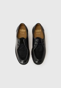 Fekete bőr, fűzős elegáns cipő, velúr panelek és bézs talpbetétek, rajta "Cléon manufacture Made in France" felirattal, fehér háttéren.