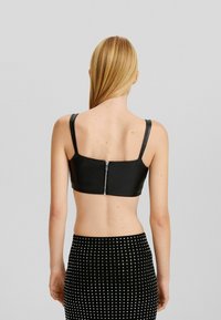 Svart fuskläderbralette med rak rygg, breda remmar och silvrig dragkedja. Matchad med en texturerad prickig kjol.